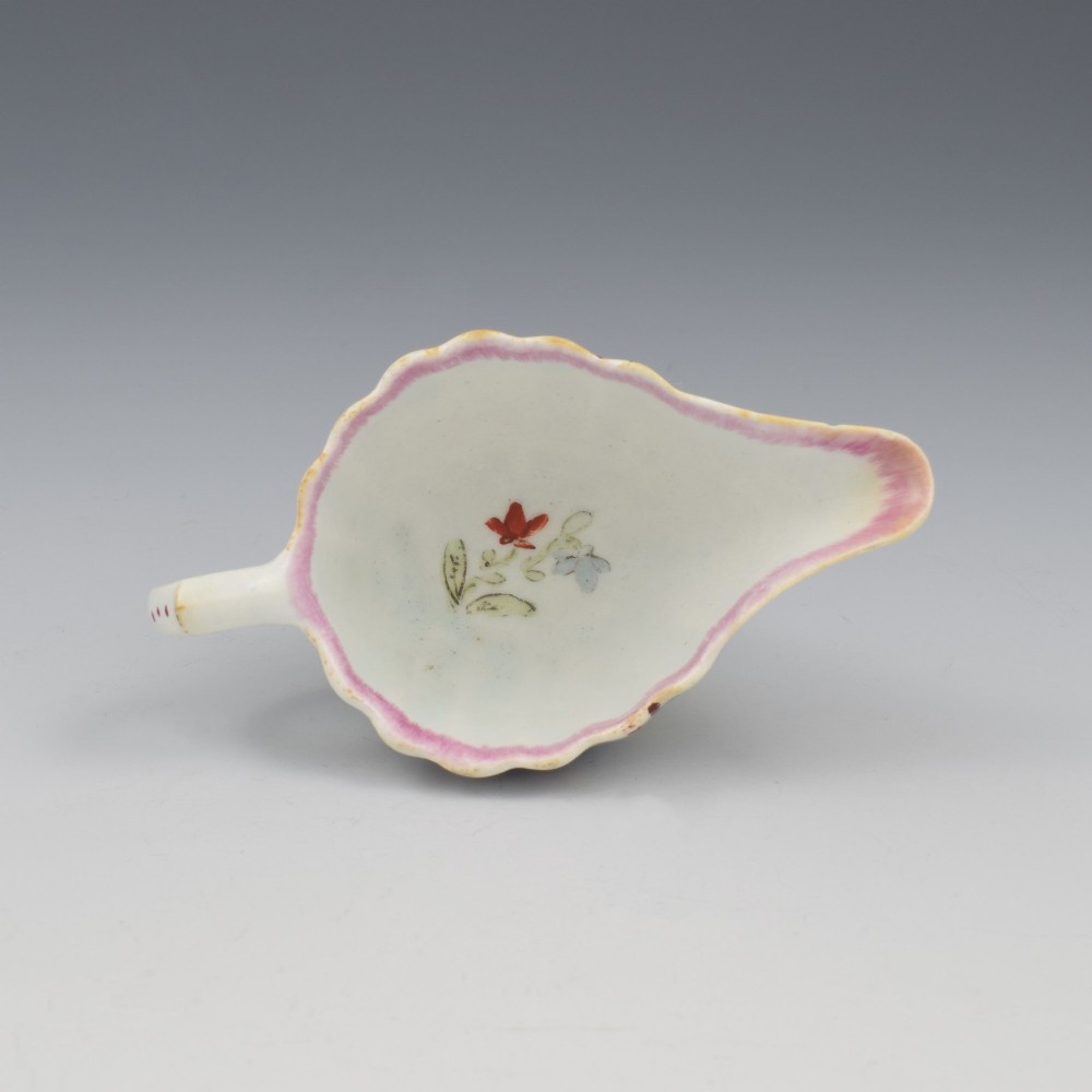 A small 18th-century soft-paste porcelain sauce boat featuring a scalloped fluted rim, loop handle, and hand-painted Chinoiserie figures with a pink interior border. View IX