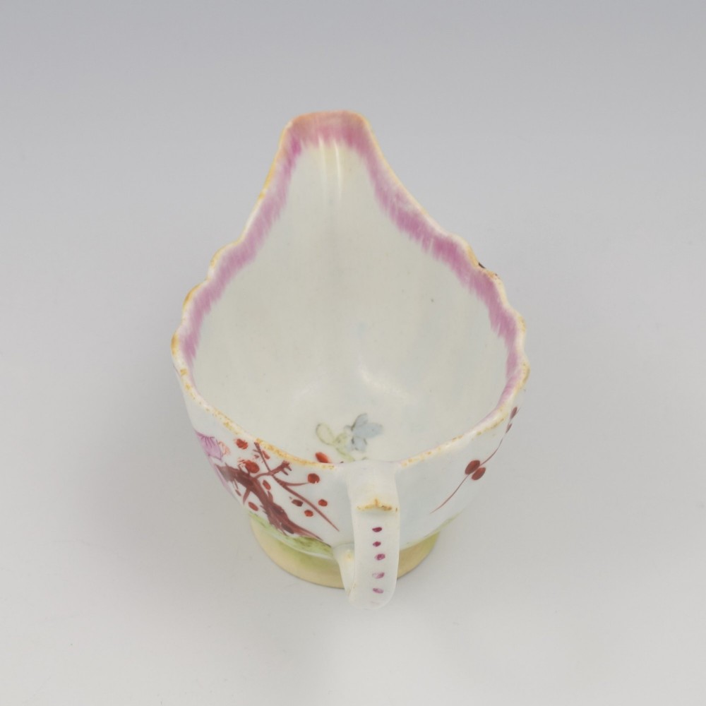 A small 18th-century soft-paste porcelain sauce boat featuring a scalloped fluted rim, loop handle, and hand-painted Chinoiserie figures with a pink interior border. View XIII