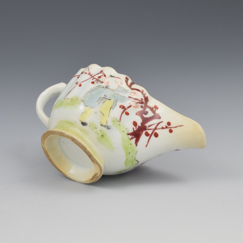 A small 18th-century soft-paste porcelain sauce boat featuring a scalloped fluted rim, loop handle, and hand-painted Chinoiserie figures with a pink interior border. View XIV