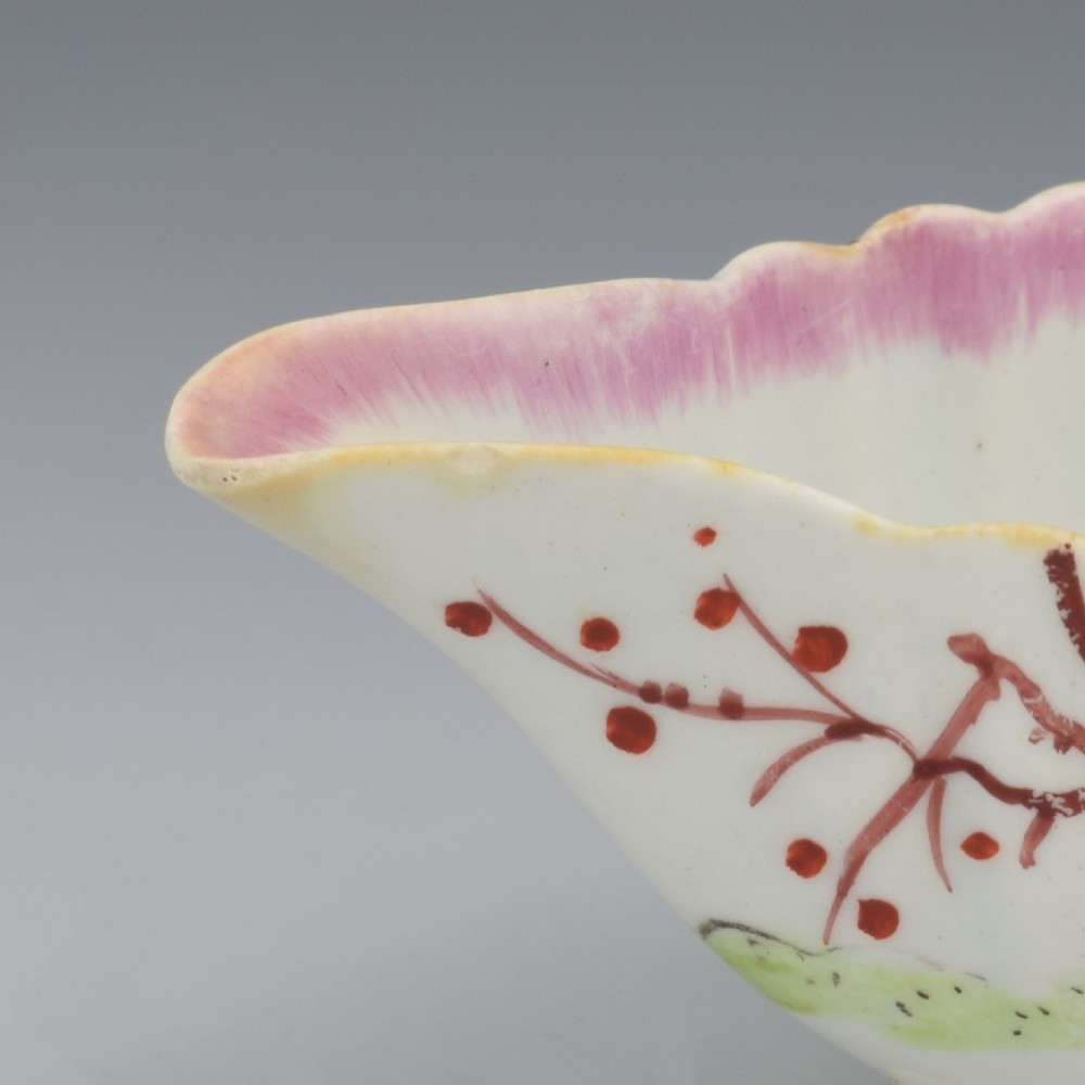 A small 18th-century soft-paste porcelain sauce boat featuring a scalloped fluted rim, loop handle, and hand-painted Chinoiserie figures with a pink interior border. View XV