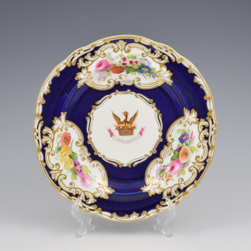 A 19th-century Copeland porcelain plate featuring a cobalt blue border with gilt scrollwork, hand-painted floral cartouches, and a central heraldic crest depicting a phoenix in flames above a coronet.