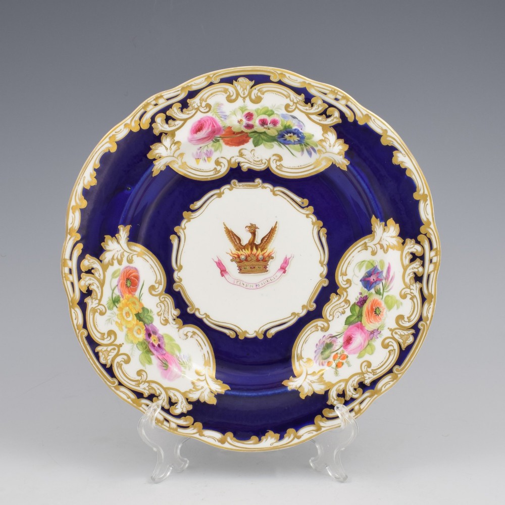 A 19th-century Copeland porcelain plate featuring a cobalt blue border with gilt scrollwork, hand-painted floral cartouches, and a central heraldic crest depicting a phoenix in flames above a coronet. View II