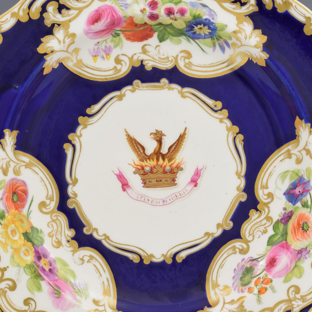 A 19th-century Copeland porcelain plate featuring a cobalt blue border with gilt scrollwork, hand-painted floral cartouches, and a central heraldic crest depicting a phoenix in flames above a coronet. View III
