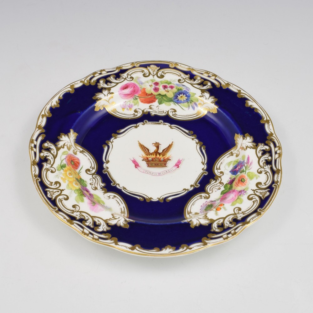 A 19th-century Copeland porcelain plate featuring a cobalt blue border with gilt scrollwork, hand-painted floral cartouches, and a central heraldic crest depicting a phoenix in flames above a coronet. View V