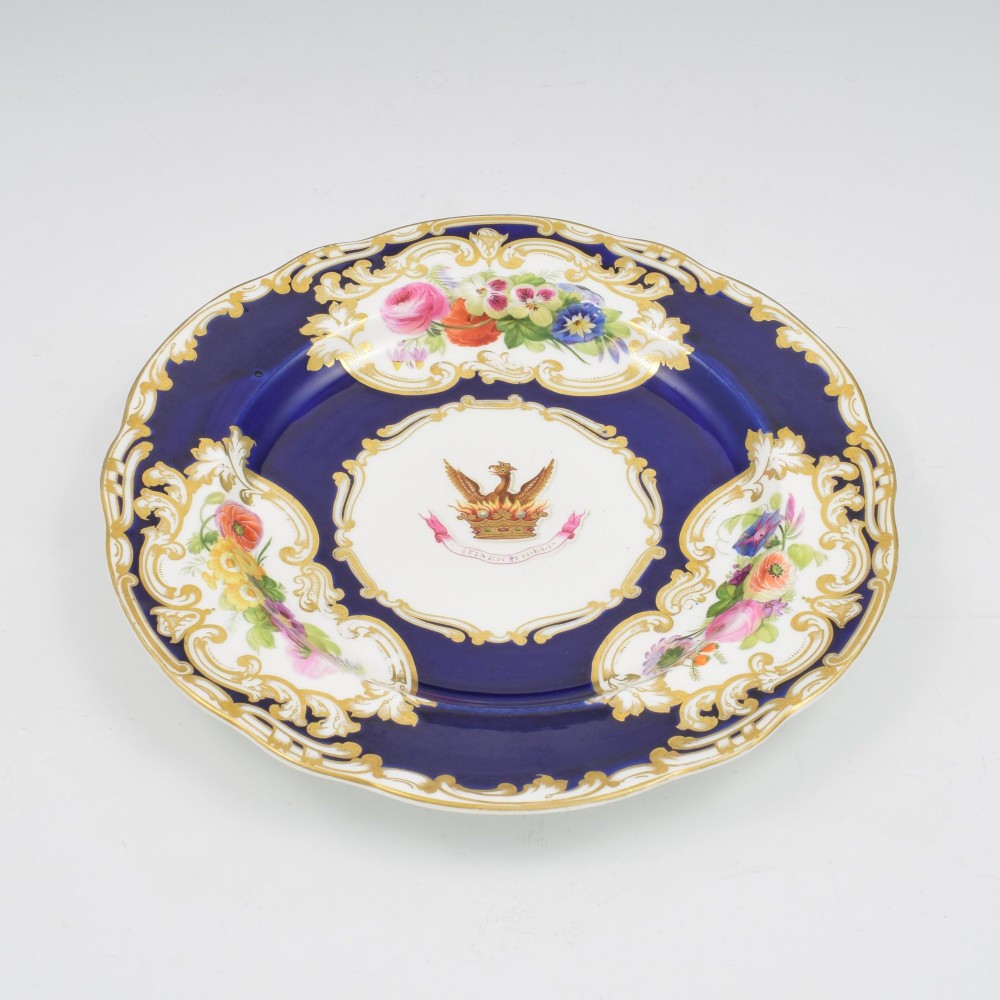 A 19th-century Copeland porcelain plate featuring a cobalt blue border with gilt scrollwork, hand-painted floral cartouches, and a central heraldic crest depicting a phoenix in flames above a coronet. View VI