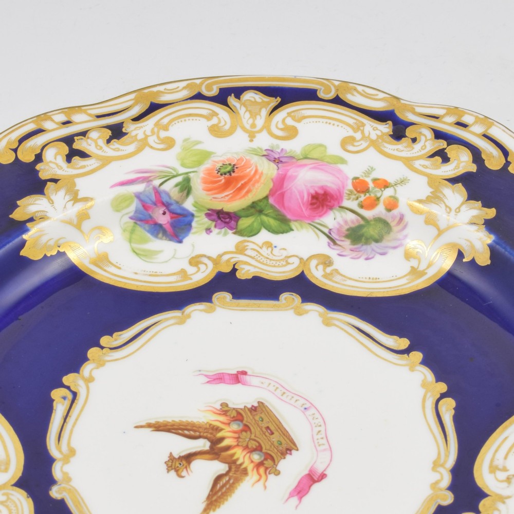 A 19th-century Copeland porcelain plate featuring a cobalt blue border with gilt scrollwork, hand-painted floral cartouches, and a central heraldic crest depicting a phoenix in flames above a coronet. View VIII