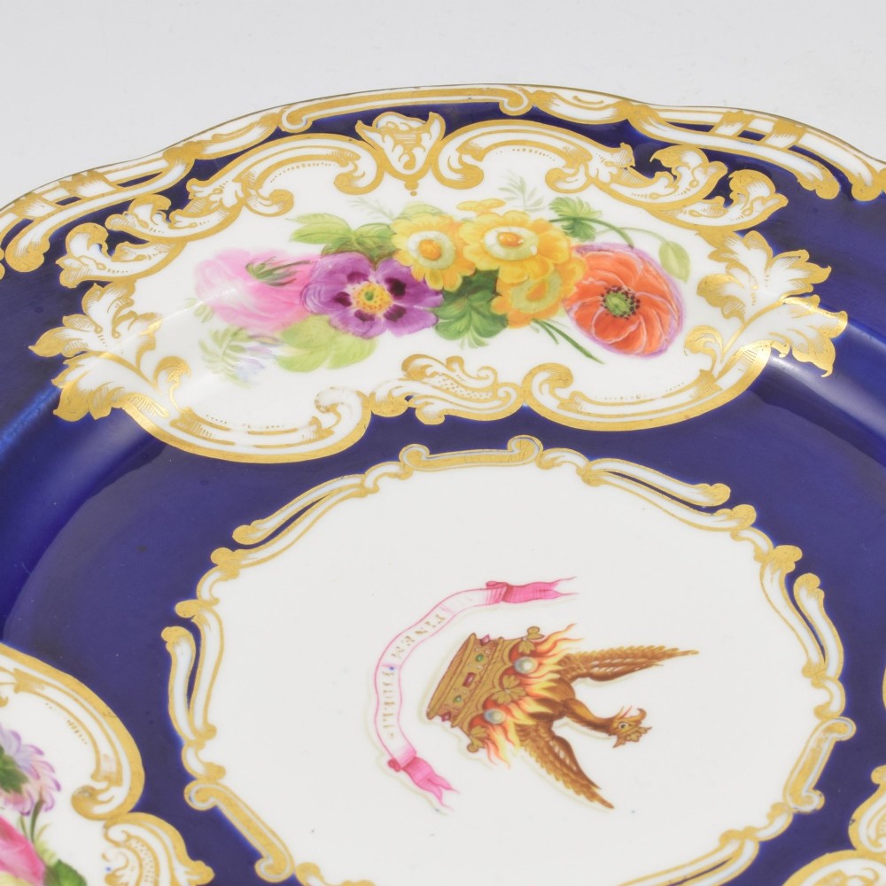 A 19th-century Copeland porcelain plate featuring a cobalt blue border with gilt scrollwork, hand-painted floral cartouches, and a central heraldic crest depicting a phoenix in flames above a coronet. View IX