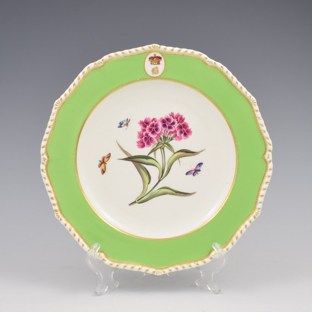 A Regency Bloor Derby porcelain plate featuring an apple green border with a marquess armorial crest, surrounding a central hand-painted illustration of pink Sweet William flowers and butterflies.