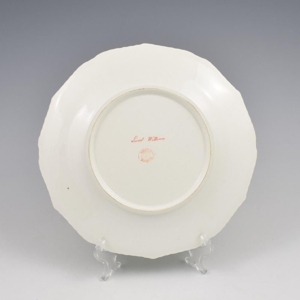 A Regency Bloor Derby porcelain plate featuring an apple green border with a marquess armorial crest, surrounding a central hand-painted illustration of pink Sweet William flowers and butterflies. View VIII