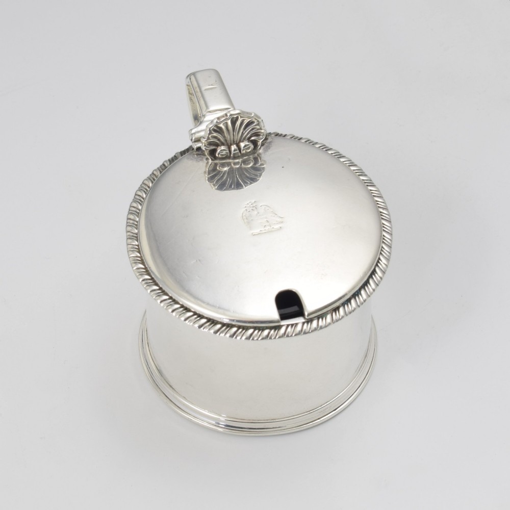 A cylindrical Georgian sterling silver drum mustard pot featuring a hinged lid, shell thumbpiece, and engraved crest. View II