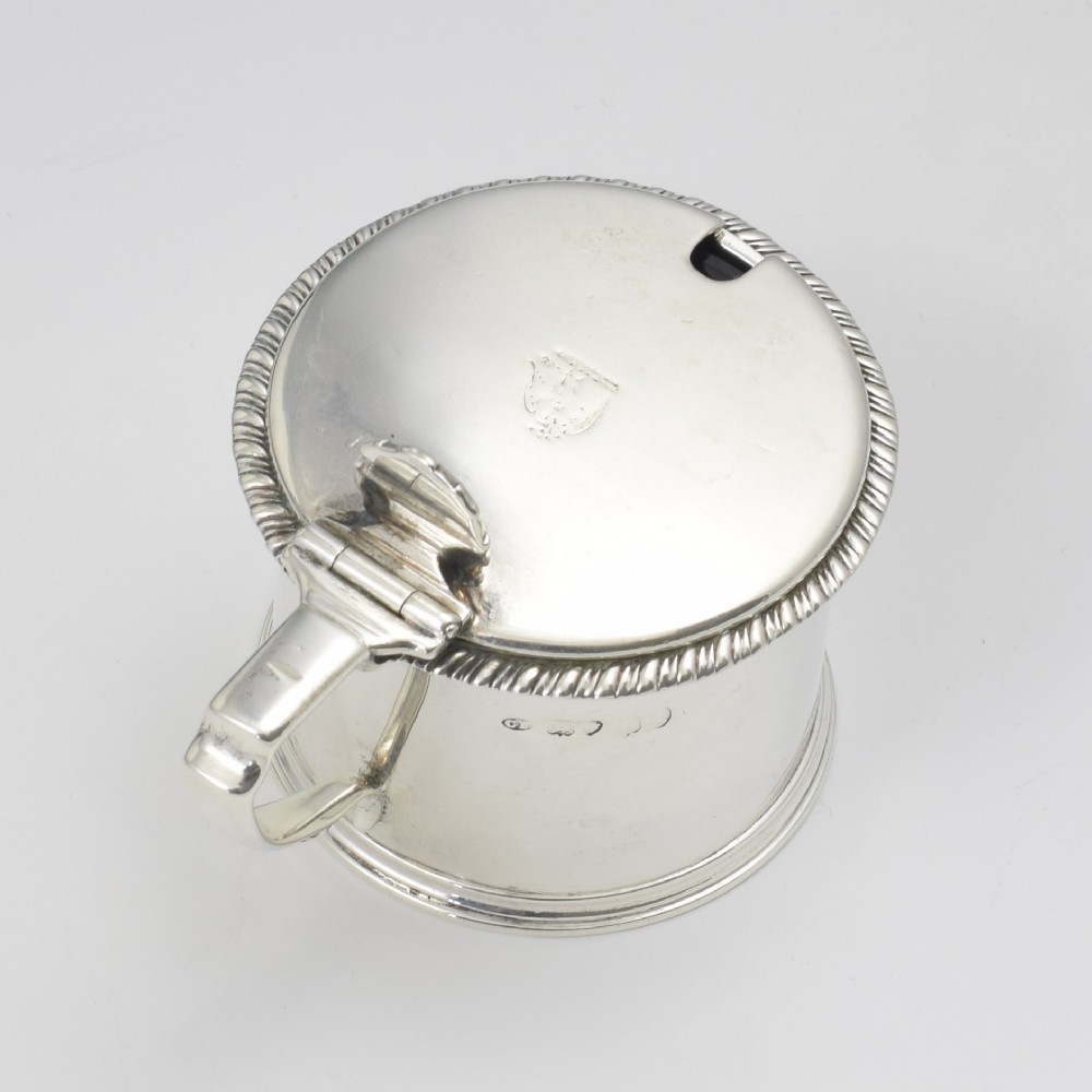 A cylindrical Georgian sterling silver drum mustard pot featuring a hinged lid, shell thumbpiece, and engraved crest. View IV