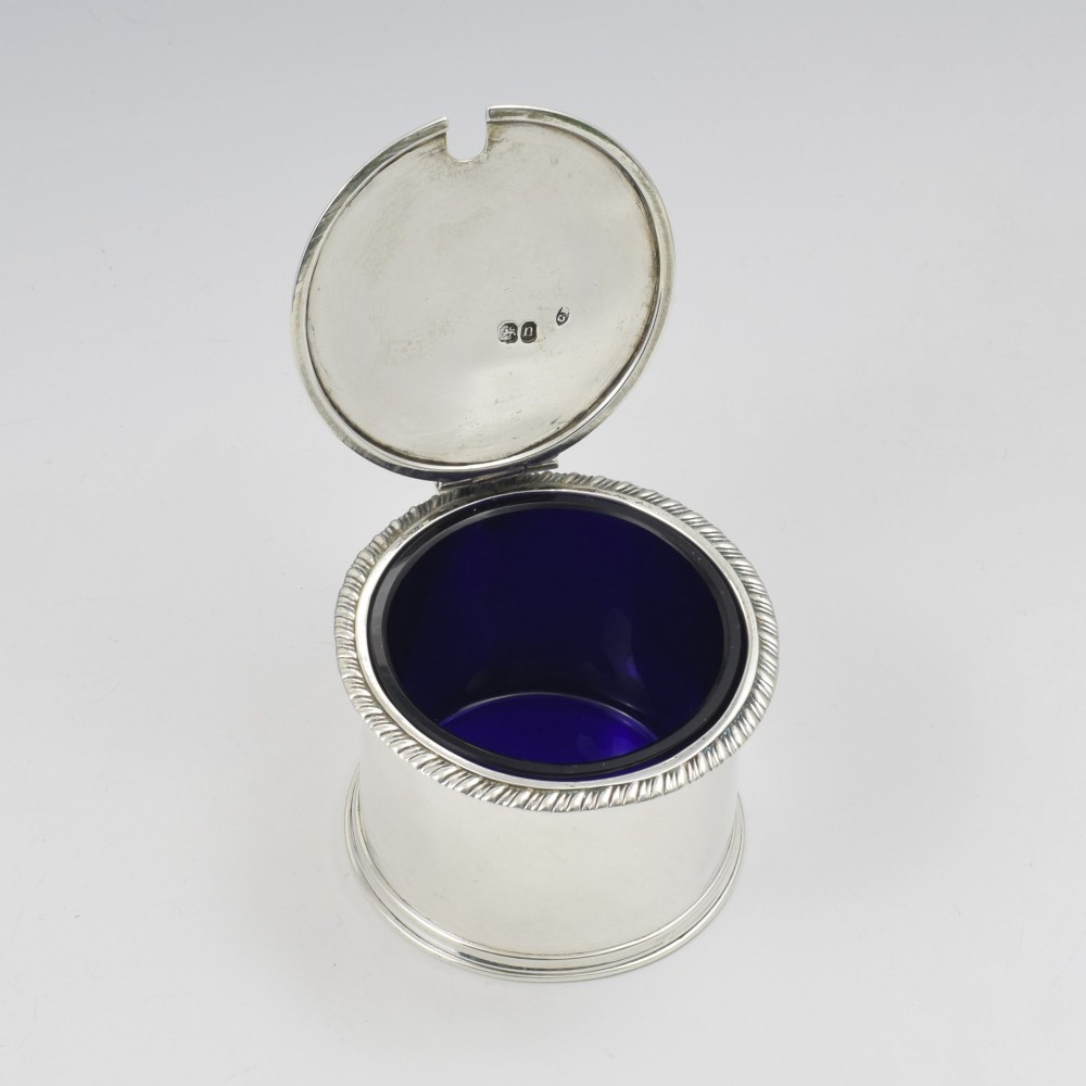 A cylindrical Georgian sterling silver drum mustard pot featuring a hinged lid, shell thumbpiece, and engraved crest. View V