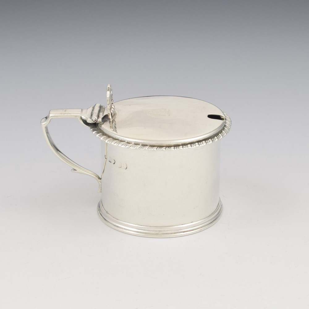 A cylindrical Georgian sterling silver drum mustard pot featuring a hinged lid, shell thumbpiece, and engraved crest. View VI