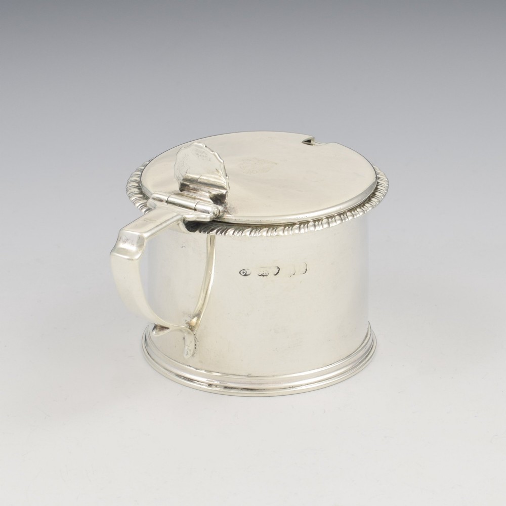 A cylindrical Georgian sterling silver drum mustard pot featuring a hinged lid, shell thumbpiece, and engraved crest. View VIII