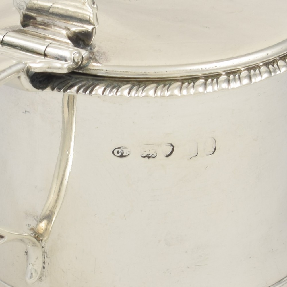 A cylindrical Georgian sterling silver drum mustard pot featuring a hinged lid, shell thumbpiece, and engraved crest. View IX