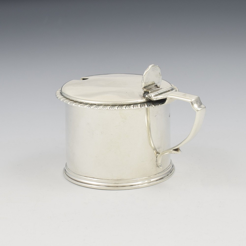 A cylindrical Georgian sterling silver drum mustard pot featuring a hinged lid, shell thumbpiece, and engraved crest. View XI