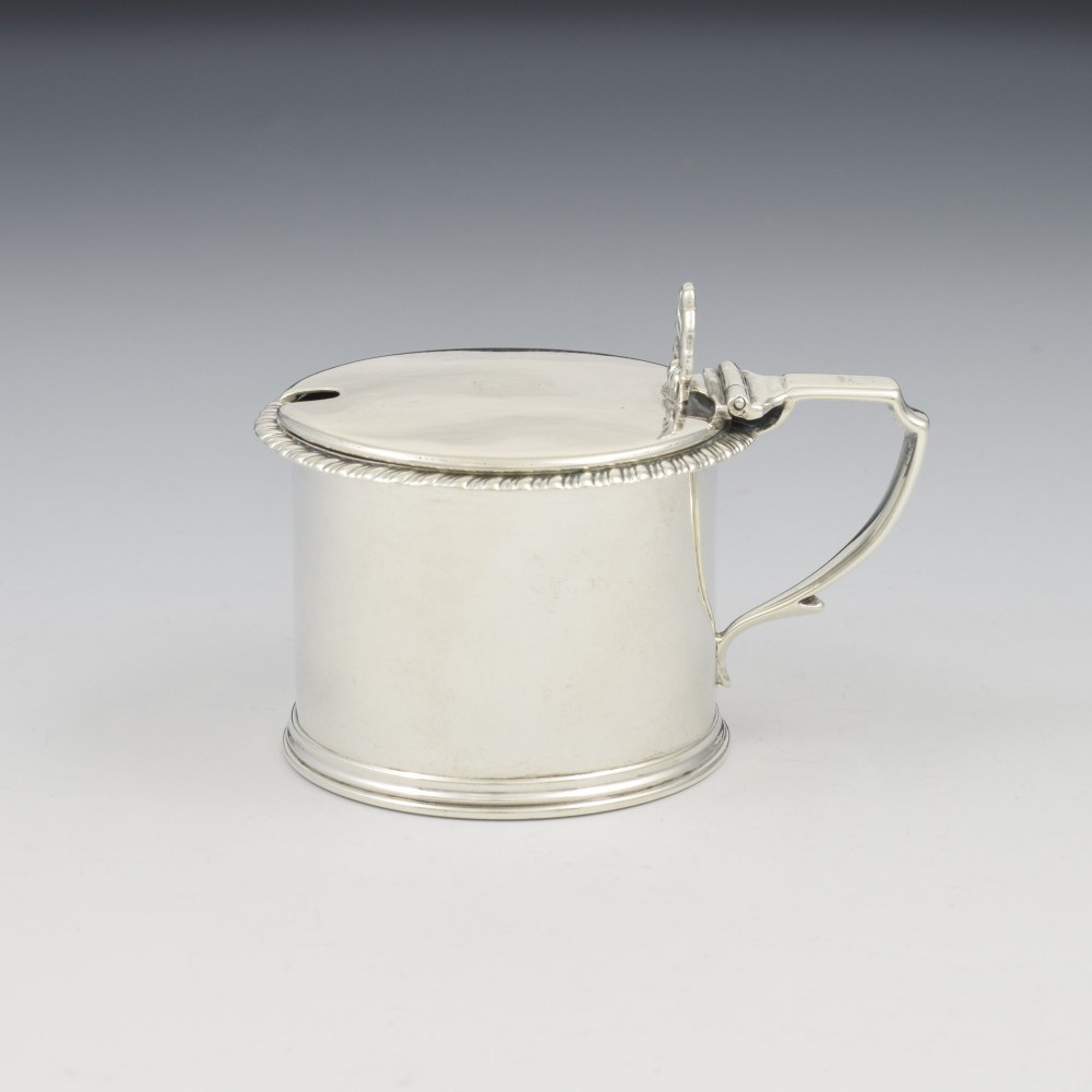 A cylindrical Georgian sterling silver drum mustard pot featuring a hinged lid, shell thumbpiece, and engraved crest. View XII