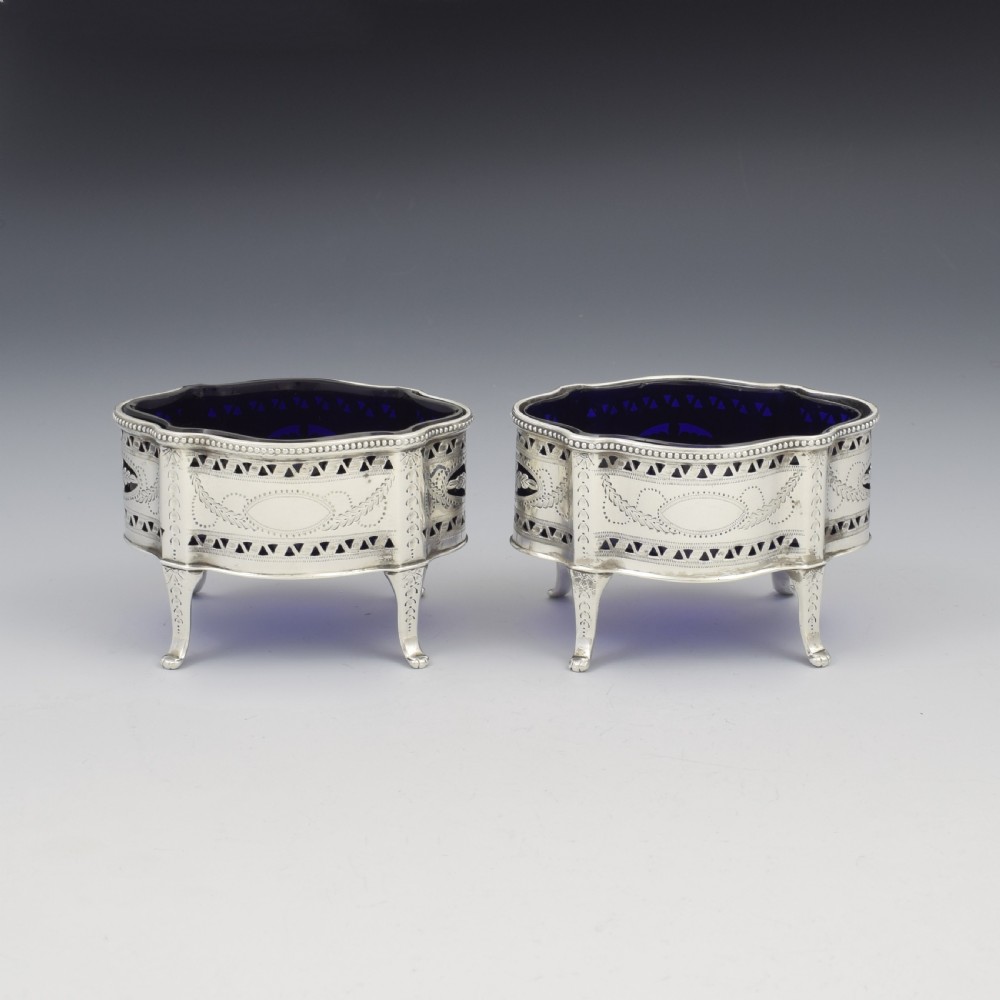 A pair of Victorian silver salt cellars with pierced serpentine frames, four feet, and cobalt blue glass liners.