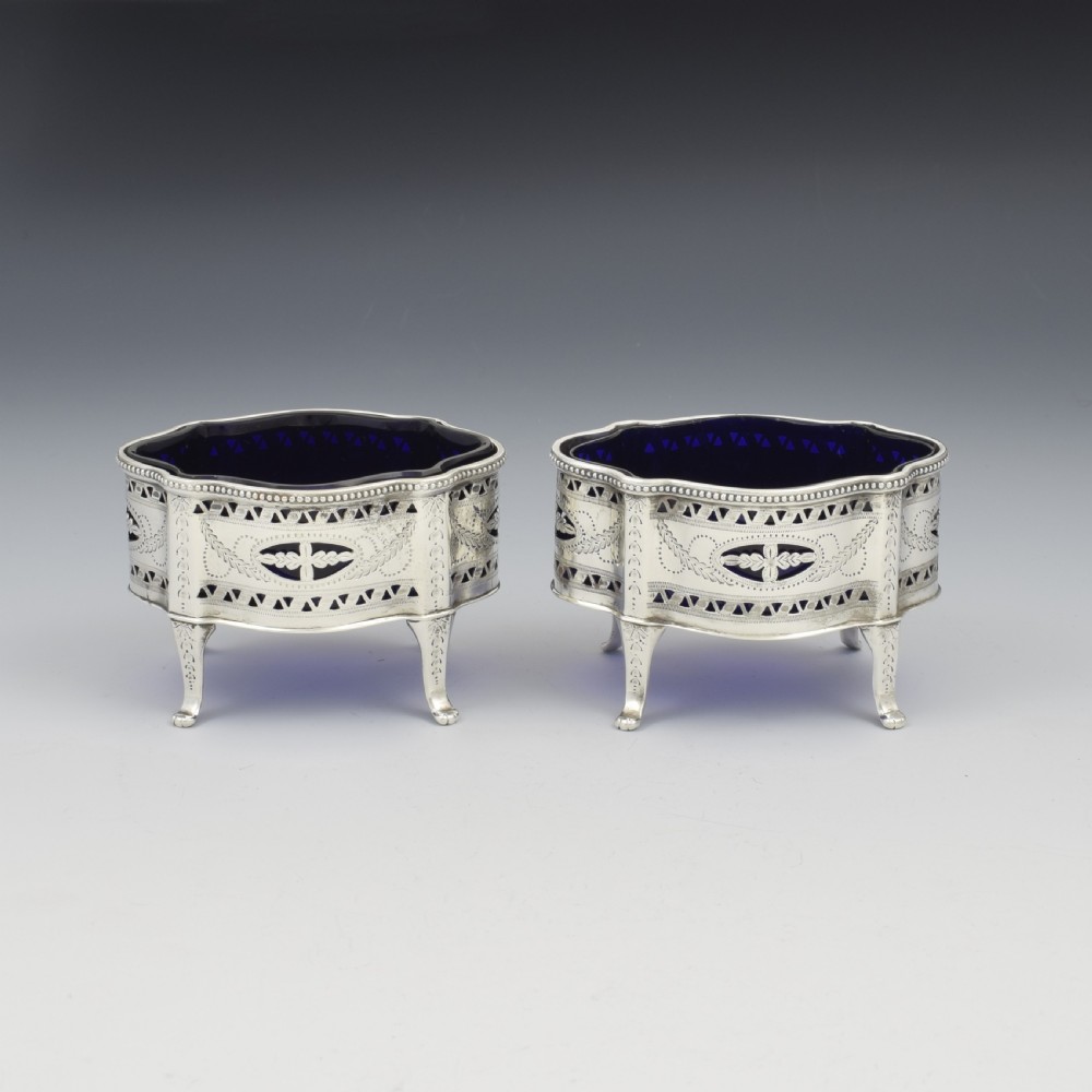 A pair of Victorian silver salt cellars with pierced serpentine frames, four feet, and cobalt blue glass liners. View IX