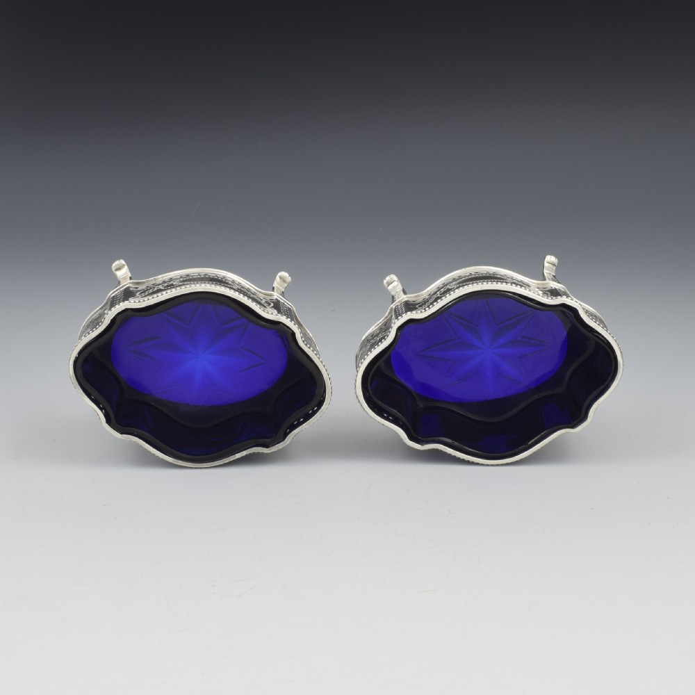 A pair of Victorian silver salt cellars with pierced serpentine frames, four feet, and cobalt blue glass liners. View XIV