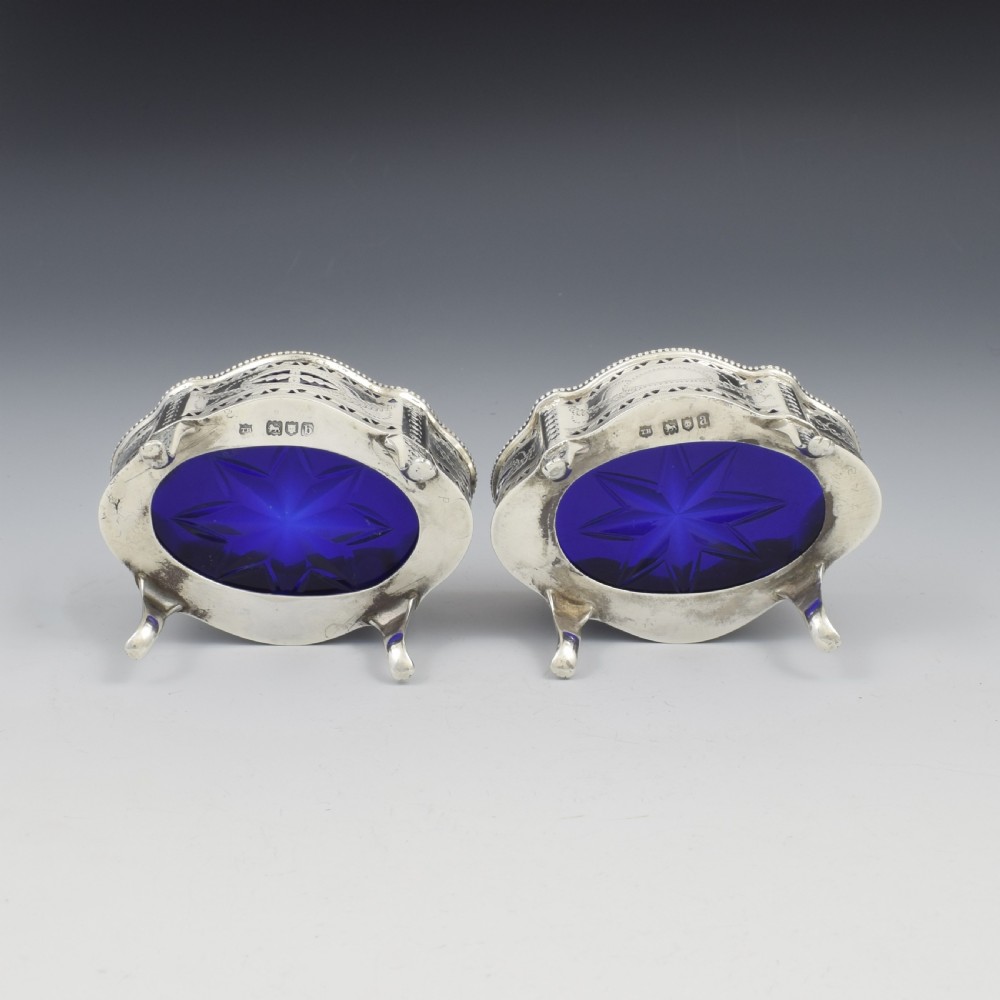 A pair of Victorian silver salt cellars with pierced serpentine frames, four feet, and cobalt blue glass liners. View XV