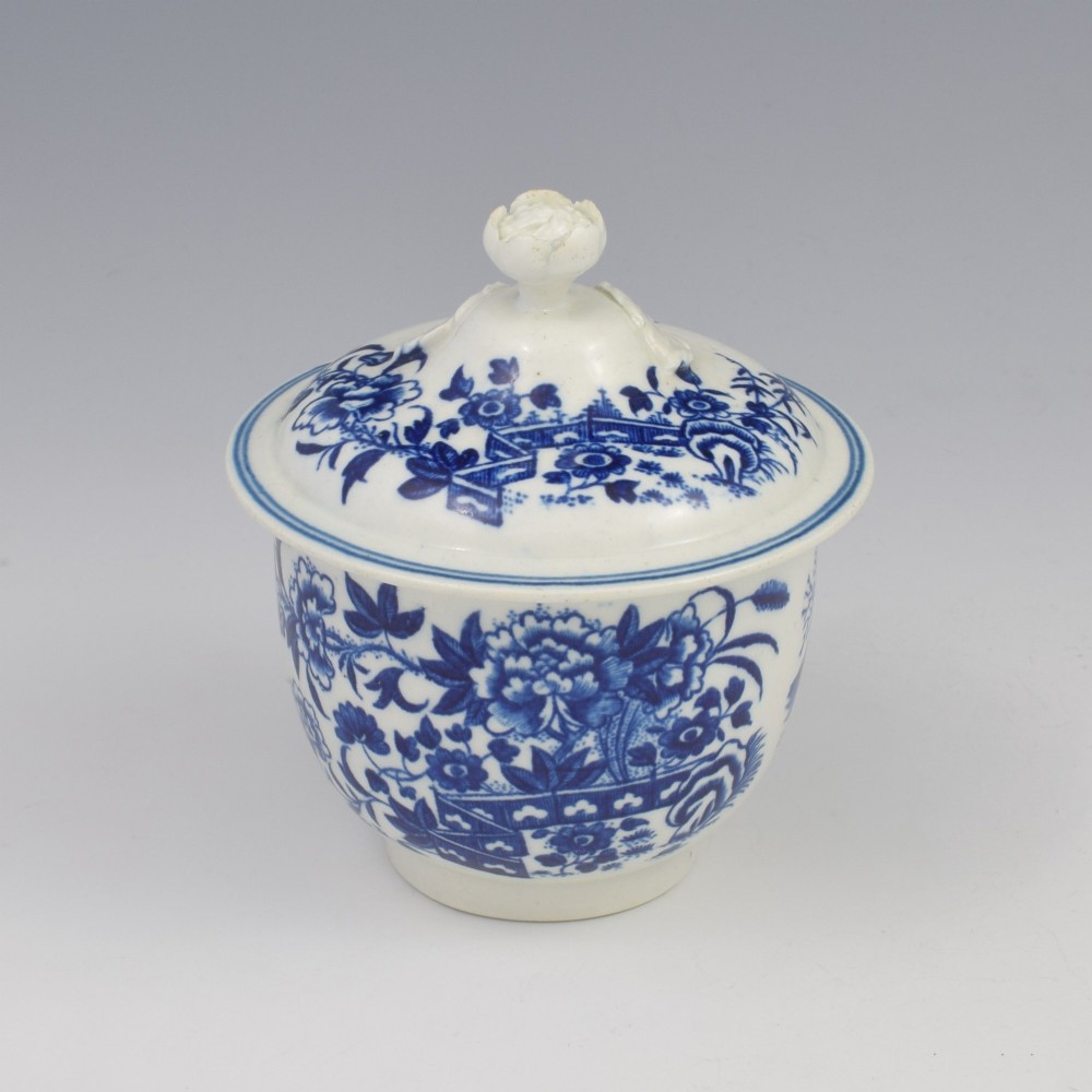An 18th-century First Period Worcester soft-paste porcelain sucrier featuring an underglaze blue transfer-printed Fence pattern with a domed cover topped by a sculpted floral finial.