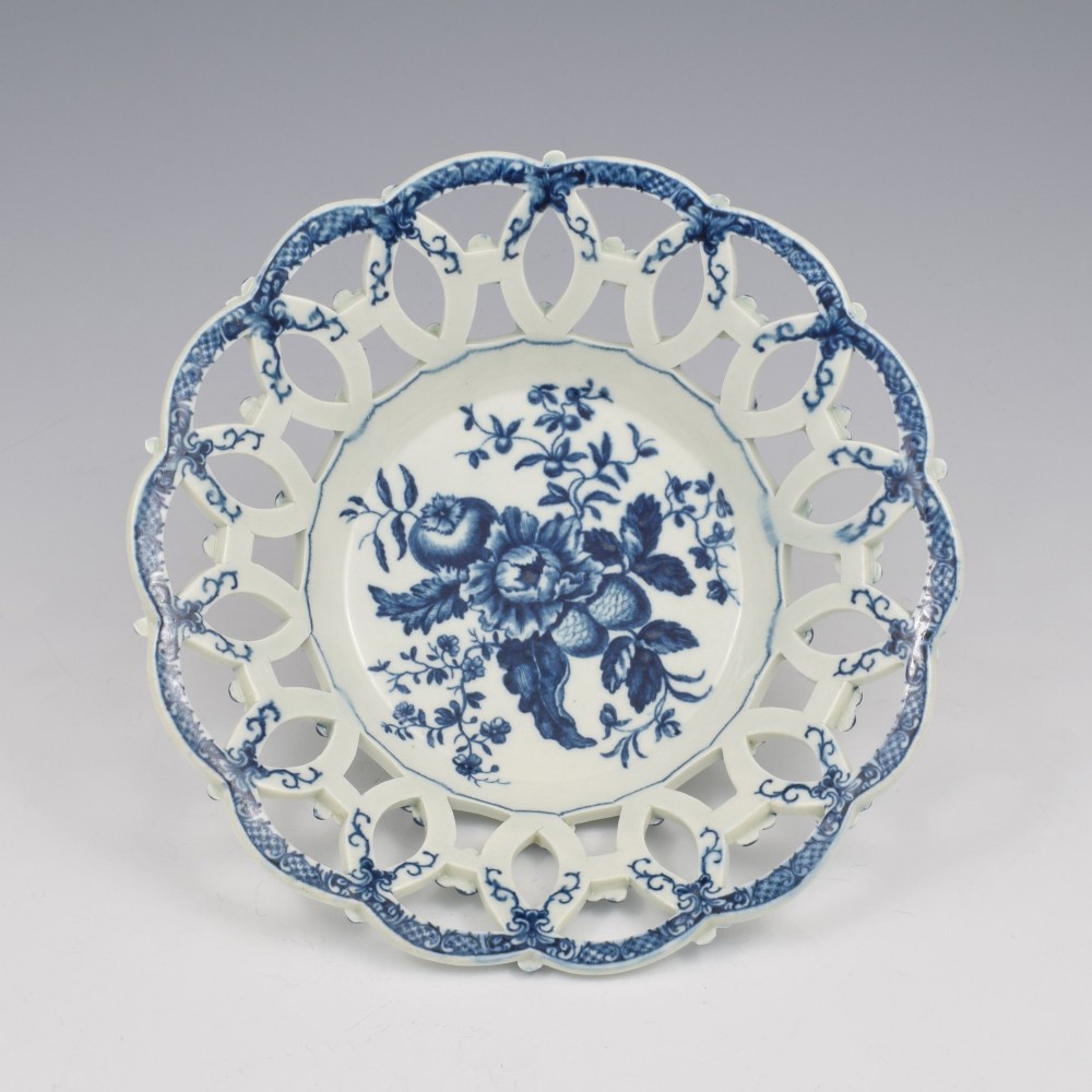 An 18th-century circular blue and white porcelain basket featuring a reticulated lattice rim and a central underglaze transfer print of flowers and pinecones.