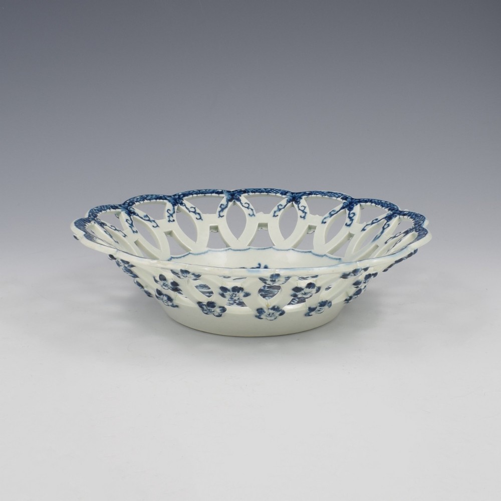 An 18th-century circular blue and white porcelain basket featuring a reticulated lattice rim and a central underglaze transfer print of flowers and pinecones. View V