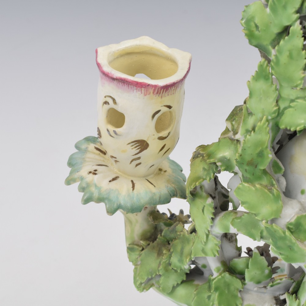 A pair of 18th-century Derby porcelain candlestick figures depicting children standing before flowering bocage trees set on scrollwork bases. View XIII