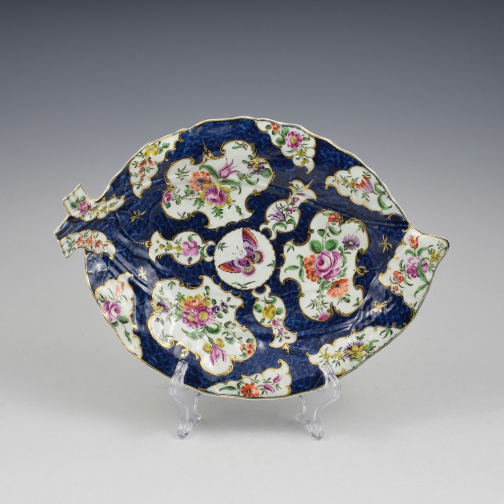 A leaf-shaped eighteenth-century Worcester porcelain dish decorated with a cobalt scale blue ground, gilded rococo reserves, floral sprays, and a central butterfly.