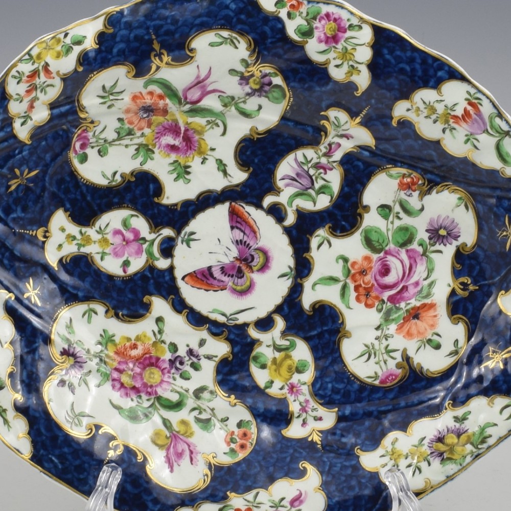 A leaf-shaped eighteenth-century Worcester porcelain dish decorated with a cobalt scale blue ground, gilded rococo reserves, floral sprays, and a central butterfly. View VI