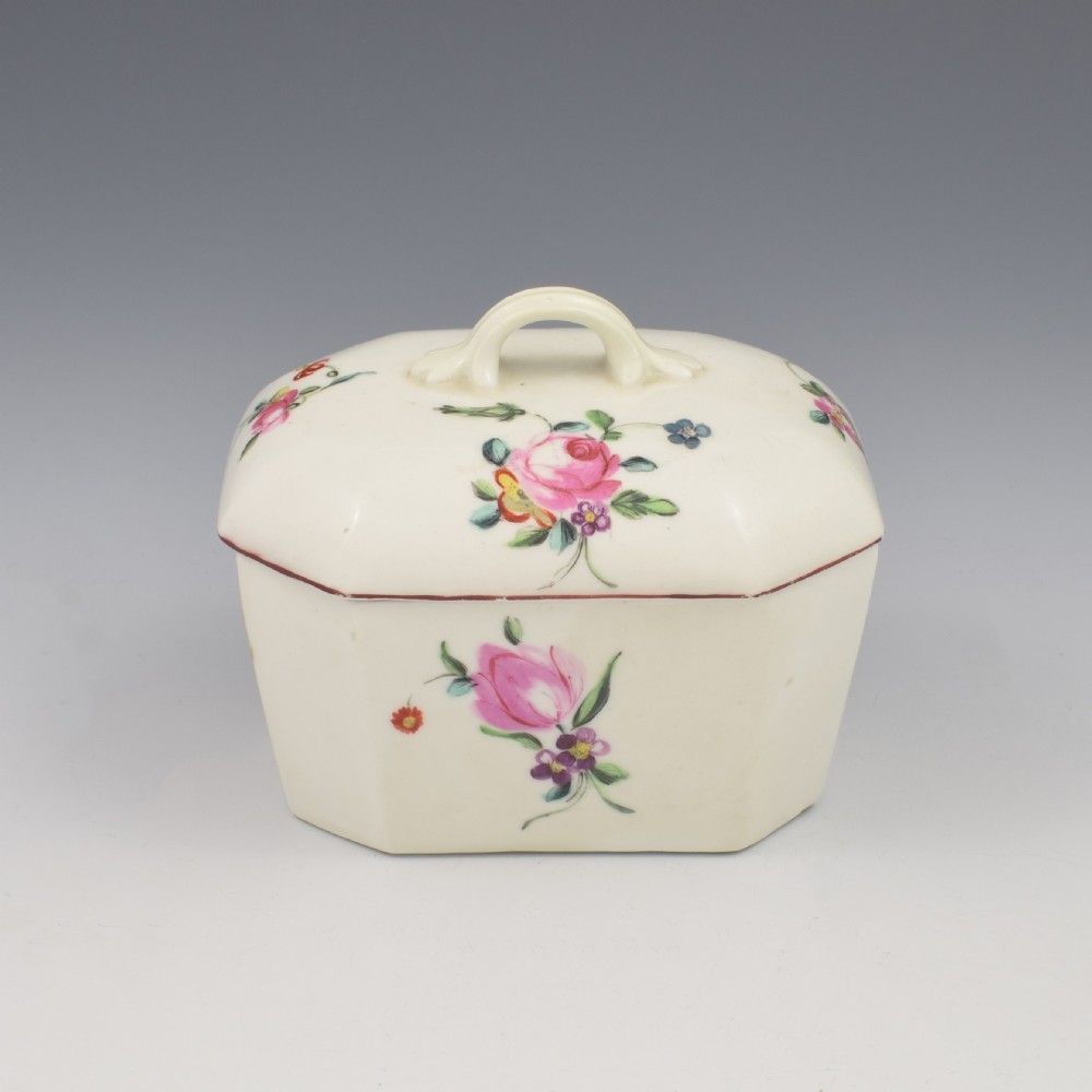 An 18th-century off-white porcelain butter tub with a fitted cover, top handle, and hand-painted floral motifs.