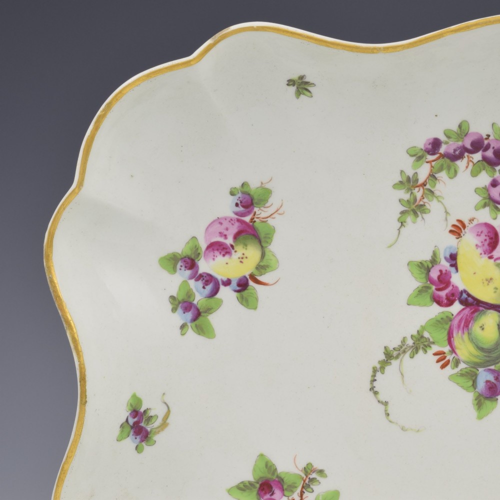 An eighteenth-century square lobed soft-paste porcelain dessert dish featuring hand-painted fruit sprays and a gilded rim. View II