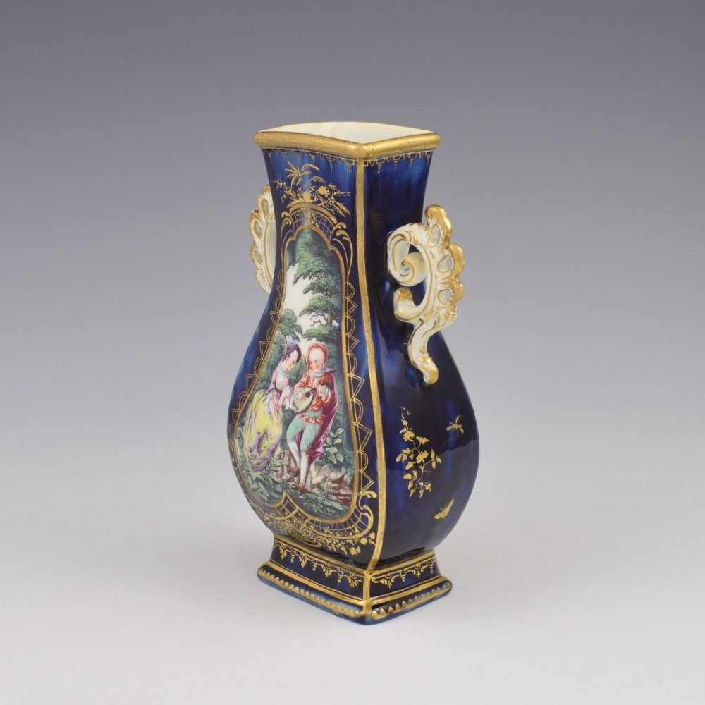 A cobalt blue soft-paste porcelain vase featuring elaborate gilt scroll handles, gilded leaf borders, and a central painted reserve depicting a gentleman playing a lute beside a lady in a landscape. View II