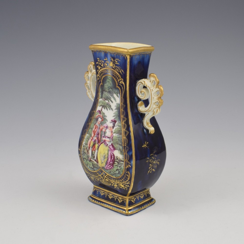 A cobalt blue soft-paste porcelain vase featuring elaborate gilt scroll handles, gilded leaf borders, and a central painted reserve depicting a gentleman playing a lute beside a lady in a landscape. View III