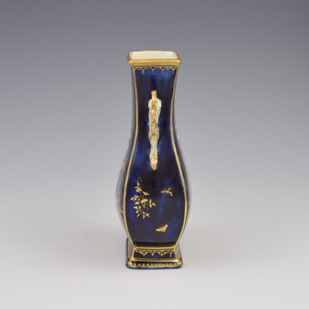 A cobalt blue soft-paste porcelain vase featuring elaborate gilt scroll handles, gilded leaf borders, and a central painted reserve depicting a gentleman playing a lute beside a lady in a landscape. View IV