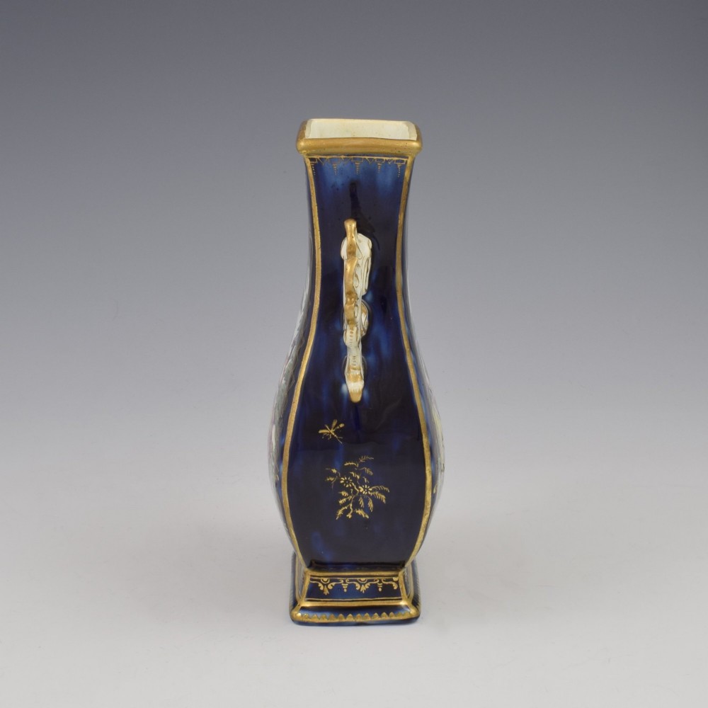A cobalt blue soft-paste porcelain vase featuring elaborate gilt scroll handles, gilded leaf borders, and a central painted reserve depicting a gentleman playing a lute beside a lady in a landscape. View V