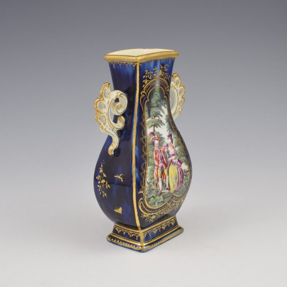 A cobalt blue soft-paste porcelain vase featuring elaborate gilt scroll handles, gilded leaf borders, and a central painted reserve depicting a gentleman playing a lute beside a lady in a landscape. View VI