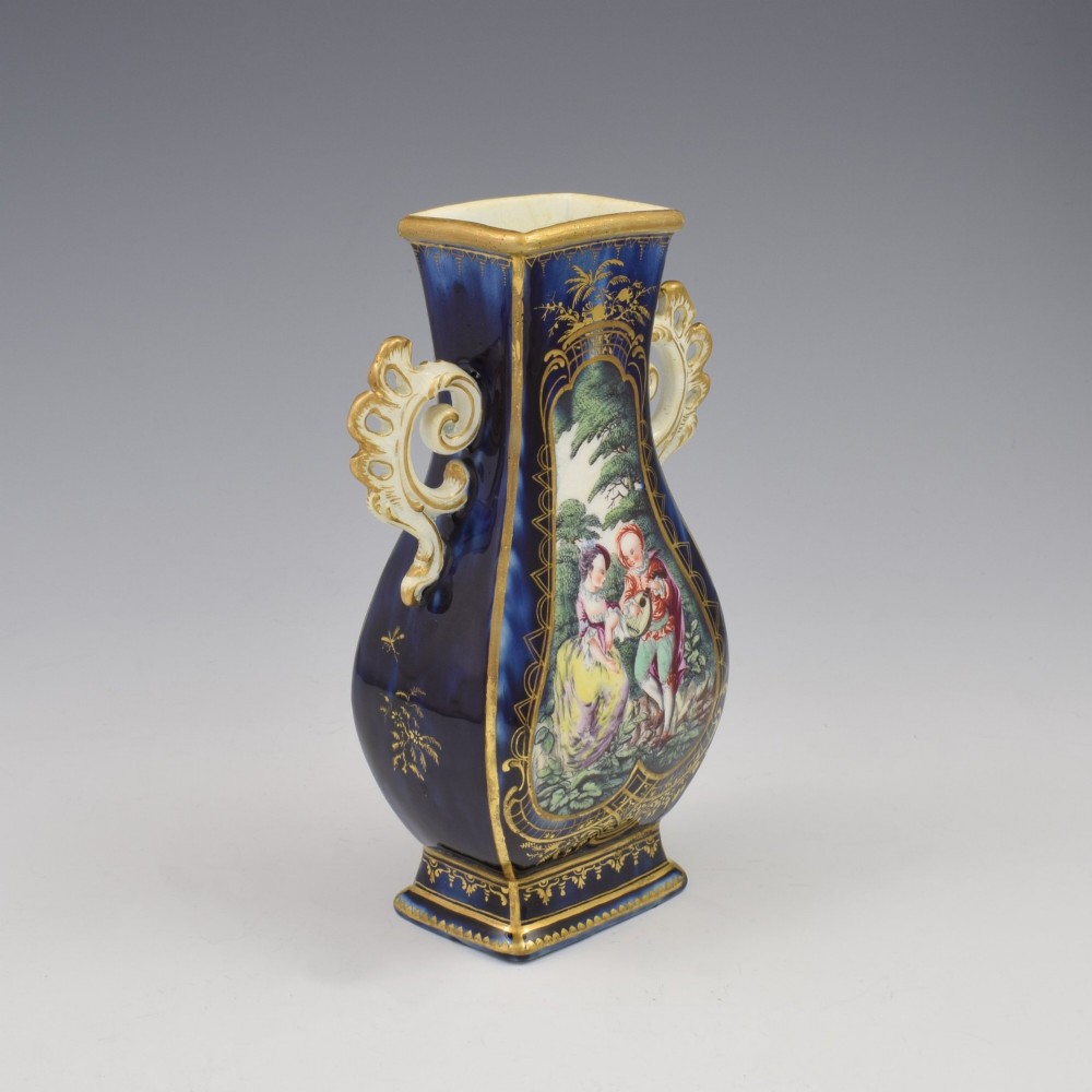 A cobalt blue soft-paste porcelain vase featuring elaborate gilt scroll handles, gilded leaf borders, and a central painted reserve depicting a gentleman playing a lute beside a lady in a landscape. View VII
