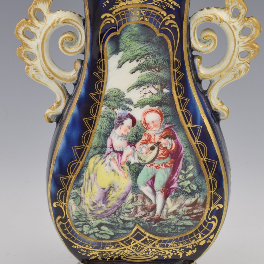 A cobalt blue soft-paste porcelain vase featuring elaborate gilt scroll handles, gilded leaf borders, and a central painted reserve depicting a gentleman playing a lute beside a lady in a landscape. View IX