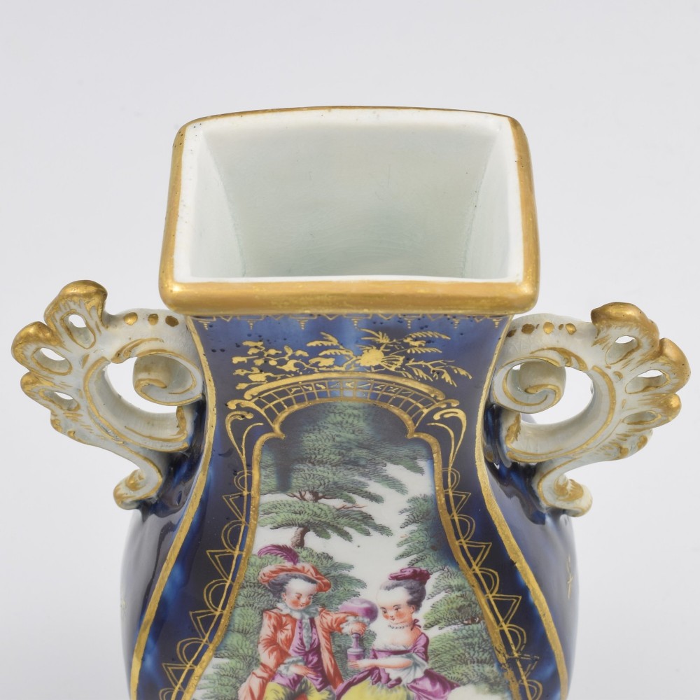 A cobalt blue soft-paste porcelain vase featuring elaborate gilt scroll handles, gilded leaf borders, and a central painted reserve depicting a gentleman playing a lute beside a lady in a landscape. View XIV