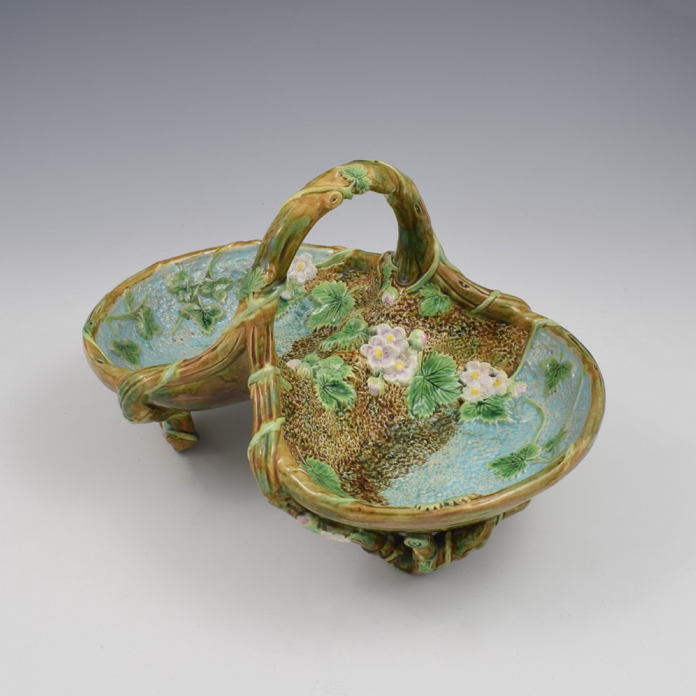 A Victorian George Jones majolica strawberry basket featuring double compartments decorated with relief leaves, pink blossoms, and an overarching branch handle in green, brown, and turquoise glazes. View II