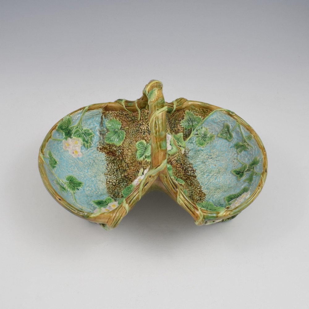 A Victorian George Jones majolica strawberry basket featuring double compartments decorated with relief leaves, pink blossoms, and an overarching branch handle in green, brown, and turquoise glazes. View VI