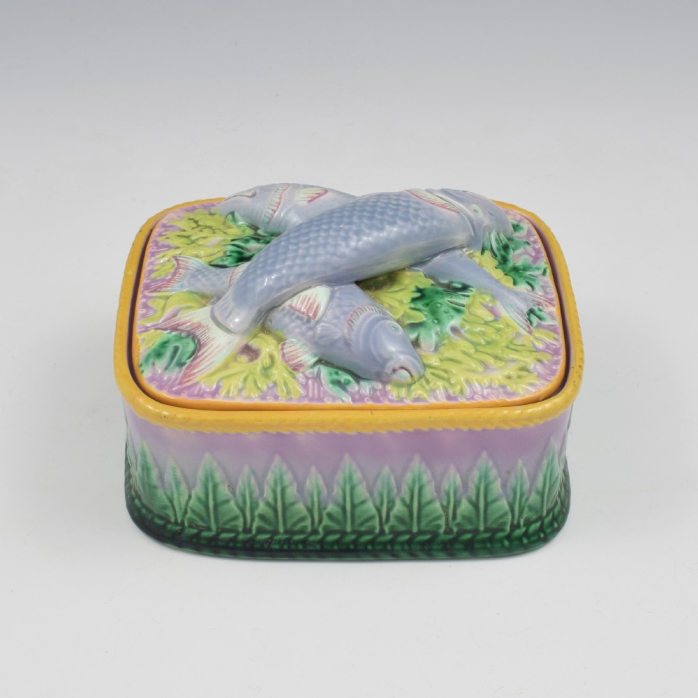 A rectangular Victorian majolica lidded box in lilac and pink featuring relief-moulded fish resting on seaweed with a yellow rim and green leaf base. View IV
