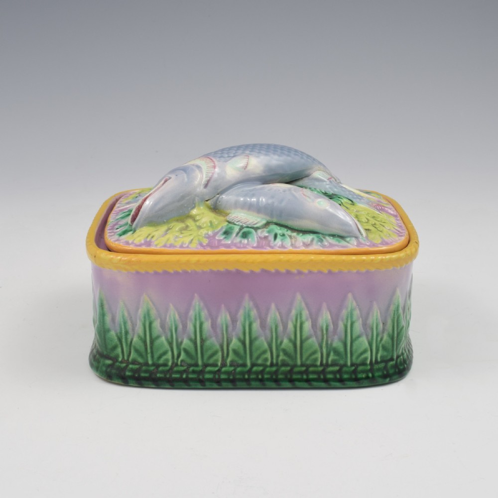 A rectangular Victorian majolica lidded box in lilac and pink featuring relief-moulded fish resting on seaweed with a yellow rim and green leaf base. View VI