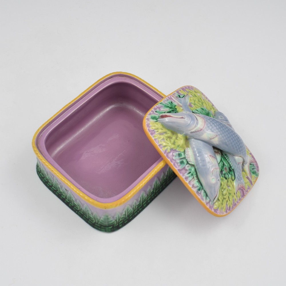 A rectangular Victorian majolica lidded box in lilac and pink featuring relief-moulded fish resting on seaweed with a yellow rim and green leaf base. View IX