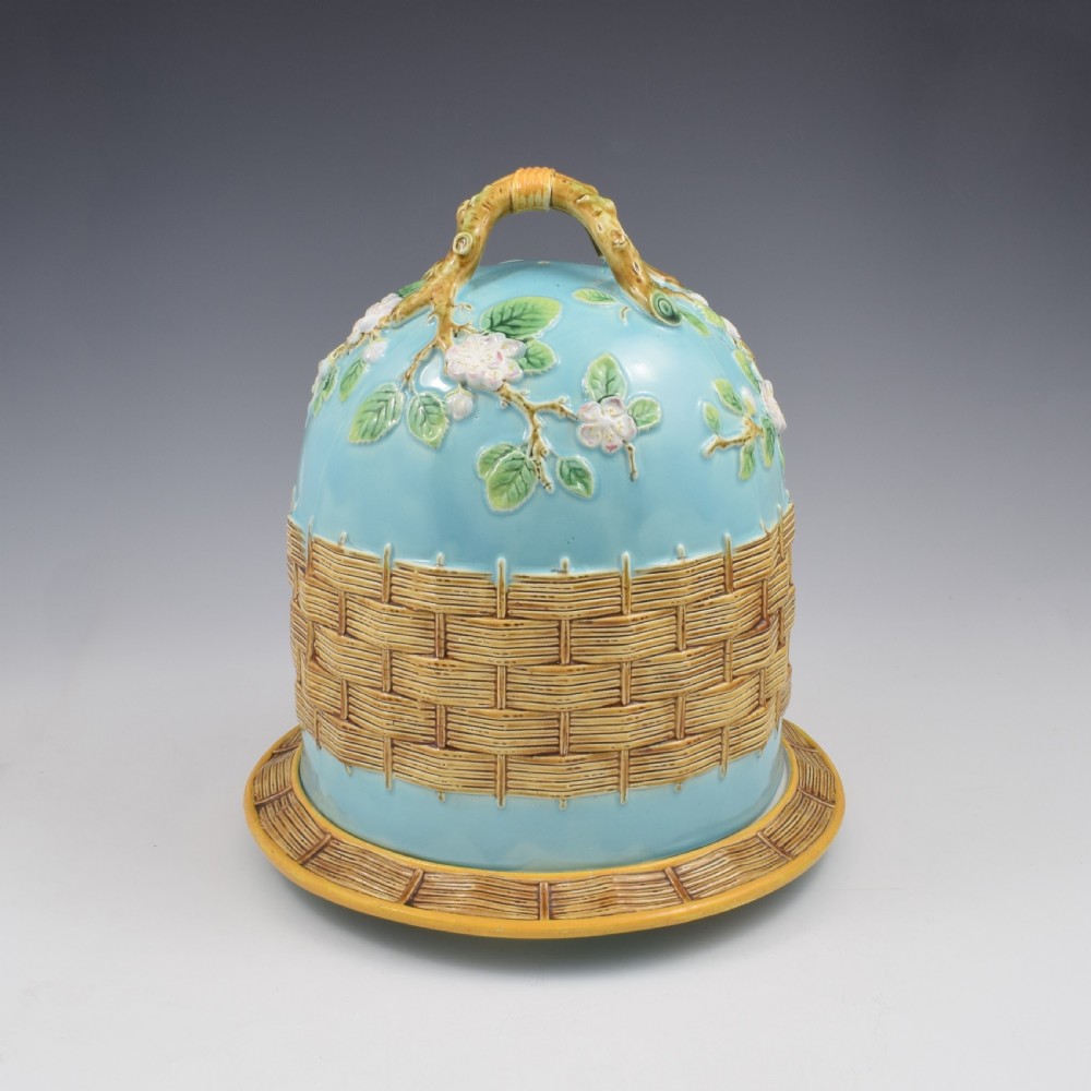A Victorian George Jones majolica cheese bell and stand featuring a turquoise dome decorated with relief apple blossoms, a woven basketweave lower band, and a twig-form handle.