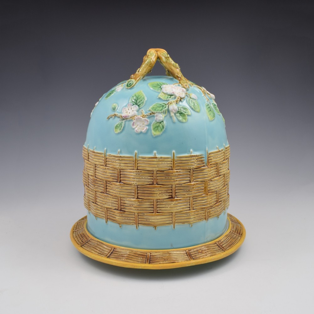 A Victorian George Jones majolica cheese bell and stand featuring a turquoise dome decorated with relief apple blossoms, a woven basketweave lower band, and a twig-form handle. View VI