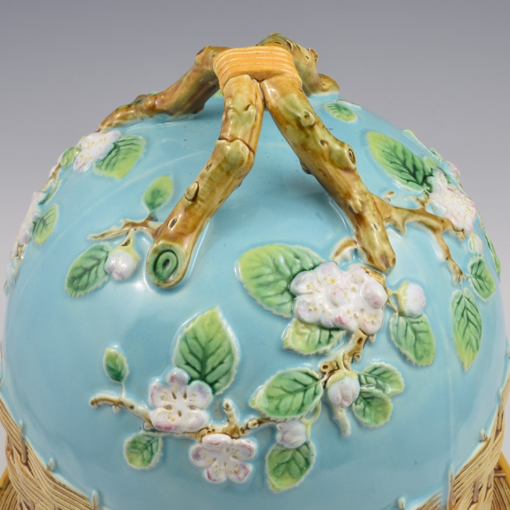 A Victorian George Jones majolica cheese bell and stand featuring a turquoise dome decorated with relief apple blossoms, a woven basketweave lower band, and a twig-form handle. View VIII
