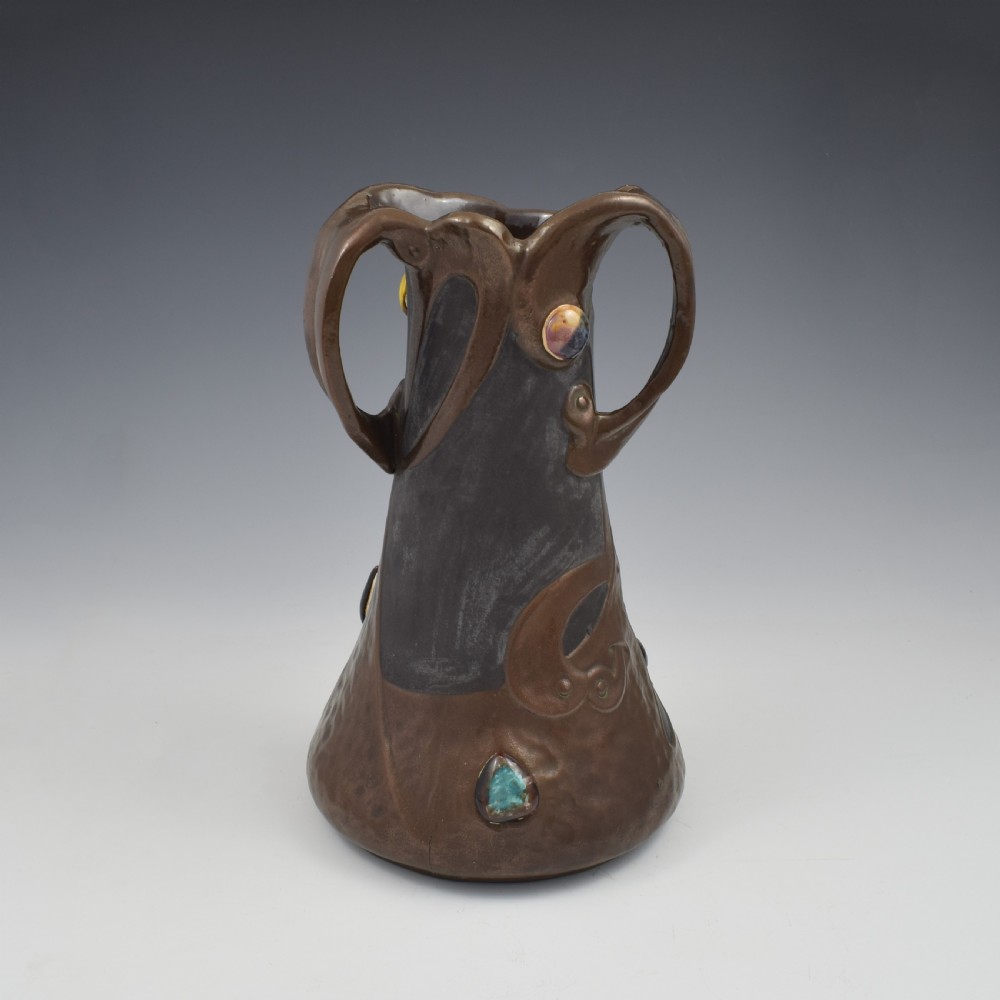 An Art Nouveau brown ceramic vase featuring a metallic copper effect surface, organic twin handles, flared rim, and inset colourful glazed cabochons. View V